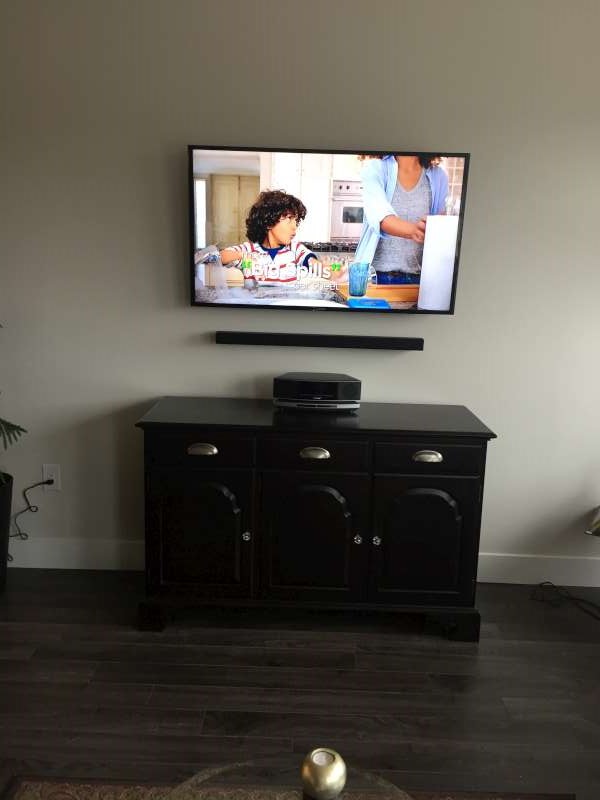 Wall-mounted TV and soundbar above a black sideboard