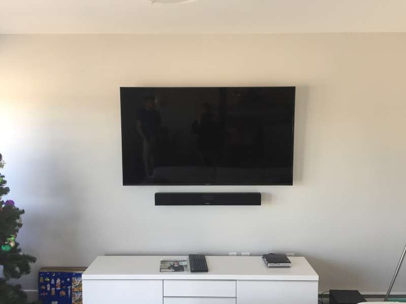 Large TV and soundbar centred on a cream wall above a white media unit