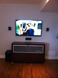 Wall-mounted TV with small surround speakers and a subwoofer