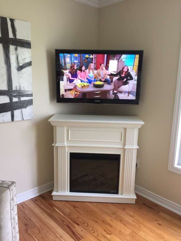 TV mounted in a room corner above a white electric fireplace